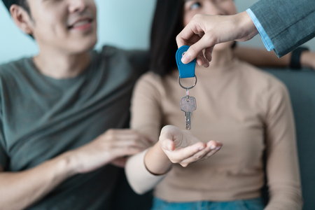 Close up of real estate agent giving keys to beautiful Asian couple of customersの写真素材