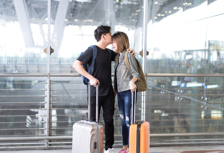 Young couple waiting with baggage near the window at the departure area of the airport.Man kissing forehead of his girlfriend.の写真素材