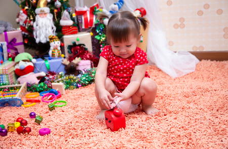 Little girl playing watch  in the living room decorated with gifts for children and a Christmas tree.の写真素材