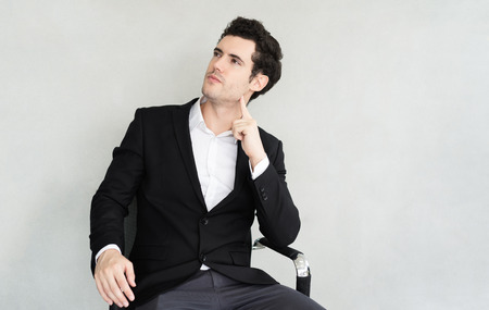 Side view portrait of handsome businessman sitting in chair at plaster texture backgroundの写真素材