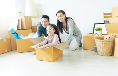 Happy young Asian family of three having fun moving with cardboard boxes in new house at moving day. Moving house day and express delivery concept.の写真素材