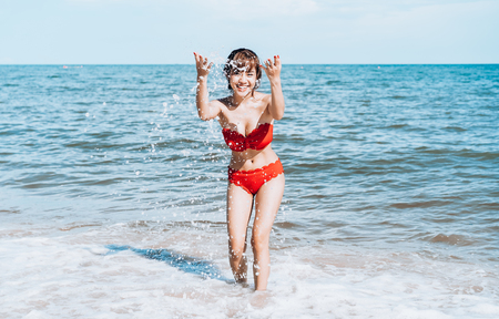 Beautiful young woman playful on paradise tropical beach having fun playing splashing water. Beach holiday and travel concept.の写真素材