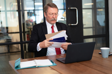 Stressed Senior Man checking bills, taxes and bank account balance in office. Debt and cost of living concept.の写真素材