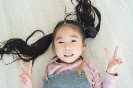 Cute pretty girl lying on the floor with showing victory gesture with both hands, looking friendly....