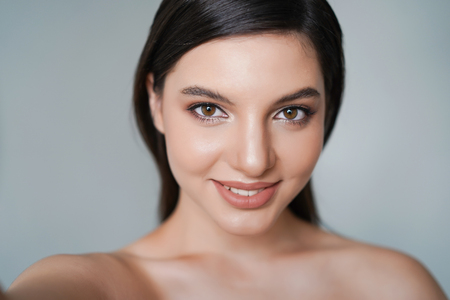 Closeup portrait of beautiful woman smiling with white teeth and making selfie on isolated over grey backgroundの写真素材