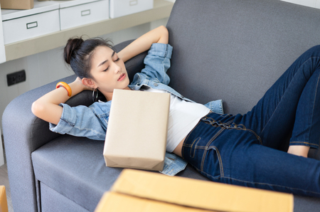 Tired young Asian businesswoman lying on the bed with packing box, Overwork load packing  box,overwork and sleep deprivation ,SME concept.の写真素材