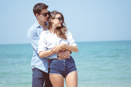 Happy Young Romantic Couple cuddling affectionate on the beach with the sea in the background.の写真素材
