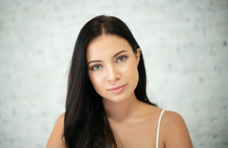 Close up portrait of natural beautiful brunette young woman against white wall.の写真素材
