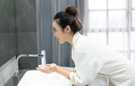 Portrait of happy young Asian woman while washing her face and  looking to mirror at bathroom.Natural skin care and people Concept.の写真素材