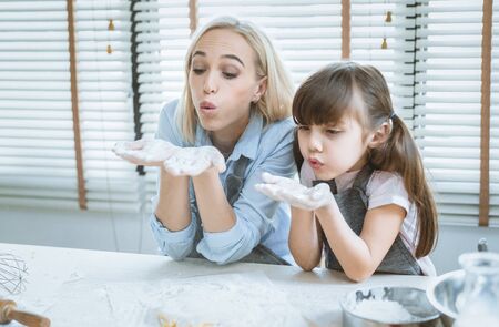 A happy family is preparing bakery together. Mother and daughter sitting at the kitchen table, a cute Blowing flour to make cookies and exciting and fun.の写真素材