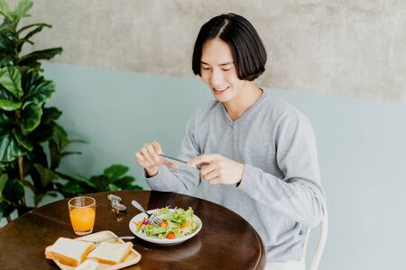 Young Asian man take a picture with mobile phone before having tasty breakfast at the kitchen table. Technology and internet addiction concept. Lifestyle, Autumn, winter season.の写真素材