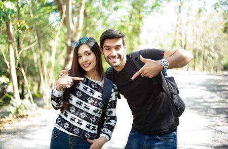 Young couple of travelers with backpacks looking at camera in the sunny forest. Adventure, travel, tourism, hike and people concept.の写真素材