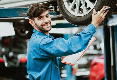 Portrait of a mechanic man in uniform with checks the machine diagnostics in car and looking at camera at auto service.  Repair of machines, fault diagnosis, repair specialist,technical maintenance and people concept.の写真素材