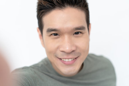 Portrait of young Asian handsome man smiling friendly and looking at camera on isolated white...