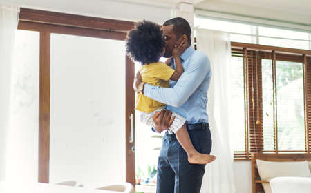 Happy family African American little son kissing his dad after going back from office. Welcome back home daddy and Sweet moments of fatherhood concept .Loving child embrace and kissing his father.の写真素材