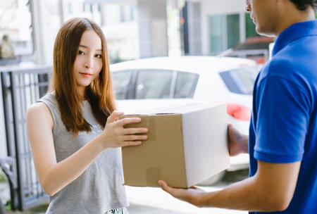 Beautiful young Asian woman receiving parcel box courier from delivery man at front of house and looking at camera.Delivery service , Onlines shopping concept.の写真素材