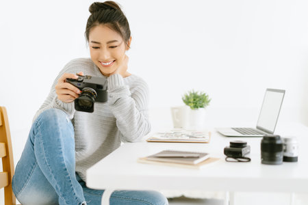 Portrait of young beautiful Asian female blogger photographer sitting at modern office while checking previews on camera.Happy Blogger and freelance work online marketing.Startup Small business owner.の写真素材