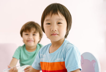 Cute little Asian boy drawing art lesson and looking at camera while his friend smile at camera in international preschool.の写真素材