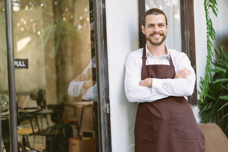 Handsome and confident cafe owner standing with his arms crossed at coffee shop door. Caucasian man...