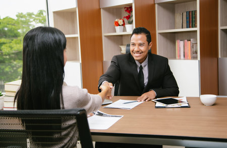 Confident insurance agent financial advisor in suit shaking hands with Asian client respect gesture....