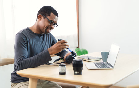 Handsome African photographer with her professional camera and cleaning the camera and lens while...