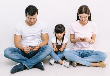 Happy technology addicted Asian family parents and kid holding smart phones having electronic...