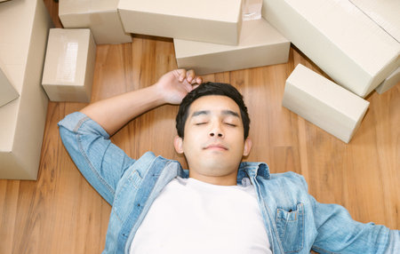 Exhausted, Tired Young Asian man working overnight and sleep on the floor with packing box feels...