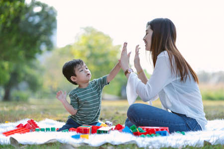Portrait of happy Asian mother and little son wearing casual style give high five and playing together in the park. Family, Kid spending time relax in holiday.の写真素材