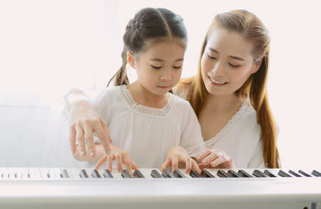 Portrait of mother Asian teaching her daughter playing a piano in living room at home. Spend time weekend together, happy mother and daughter. Creating activities to strengthen skills for children.の写真素材