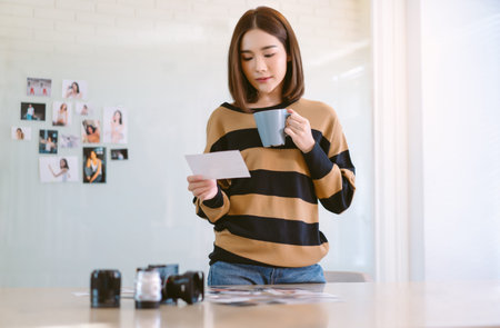 Beautiful Asian woman photographer work in her studio. Freelancer Korean or Japanese female drinking...