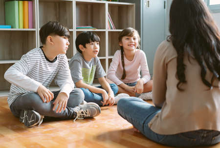 Multiethnic group of Elementary School kids sitting on floor in circle around near female teacher listen story in classroom. Education, elementary school, learning Conceptの写真素材