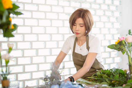 Asian woman vlogger influencer or SME owner florist creating beautiful bouquet in flower shop. Smiling millennial beautiful female in apron working at flower shop market. Startup Small business owner.の写真素材