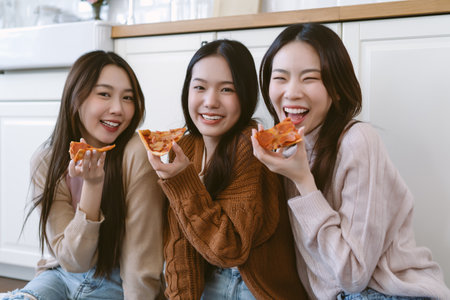 Smiling young Asian hipster female friends eating ordered pizza in kitchen room. Happy Korean girls reunion meeting, talking, laughing, spending time together on weekend. Fast delivery food conceptの写真素材