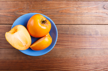 Ripe orange persimmon in a blue plate, on brown woodenの写真素材