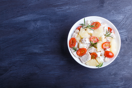 Chicken fillet salad with rosemary, pineapple and cherry tomatoes on dark blue woodenの写真素材