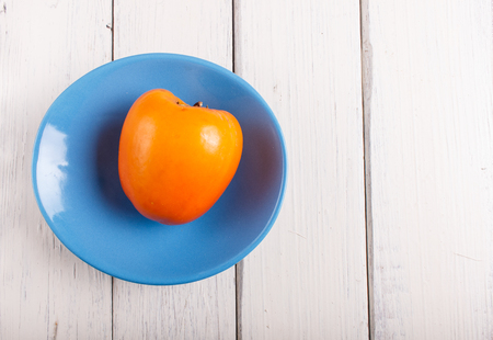 Ripe orange persimmon in a blue plate on white woodenの写真素材