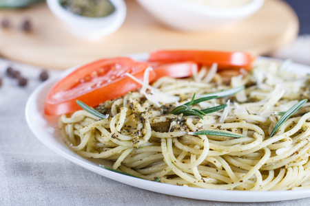 Spaghetti pasta with pesto sauce, tomatoes and cheese on a linen tablecloth. close up, selective focus.の写真素材