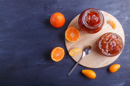 Tangerine and kumquat jam in a glass jar with fresh fruits on a black wooden table. Homemade, copy space, top view.の写真素材