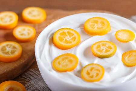 greek yogurt with kumquat pieces in a white plate on a brown wooden background, close up.の写真素材