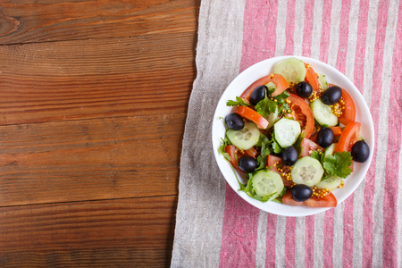 Vegetarian salad of tomatoes, cucumbers, parsley, olives and mustard on linen tablecloth, top view, flat lay, copy space. brown wooden background.の写真素材