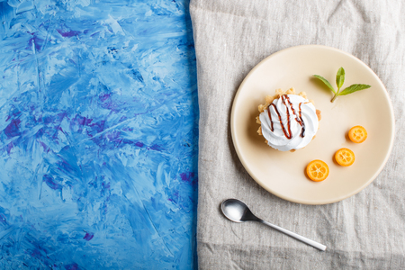 Cake with whipped egg cream on a light brown plate with kumquat slices and mint leaves on a blue concrete background with linen napkin. copy space, flat lay, top view.の写真素材