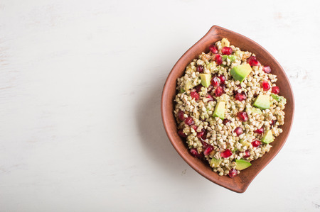 Salad of germinated buckwheat, avocado, walnut and pomegranate seeds in clay plate on white wooden background. Top view, copy space.の写真素材