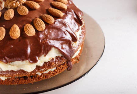 Homemade chocolate cake with milk cream, caramel and almonds on white wooden background. close up.