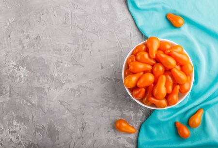 Fresh orange grape tomatoes in white ceramic bowl on gray concrete background with blue textile. top view, flat lay, copy space.の写真素材