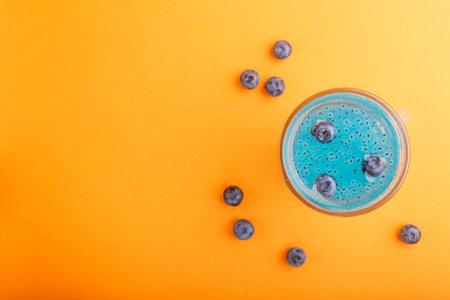 Glass of blueberry blue colored drink with basil seeds on orange background. Morninig, spring,...