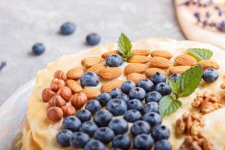 Homemade layered Napoleon cake with milk cream. Decorated with blueberry, almonds, walnuts, hazelnuts, mint on a gray concrete  background. side view, selective focus, close up.の写真素材