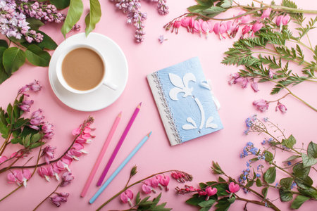Purple lilac and bleeding heart  flowers and a cup of coffee with notebook and colored pencils on...