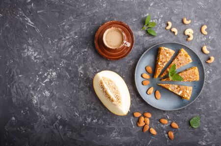 Traditional turkish candy cezerye made from caramelised melon, roasted walnuts, hazelnuts, cashew, pistachios in blue ceramic plate and a cup of coffee on a black concrete background. top view, flat lay, copy space.の写真素材