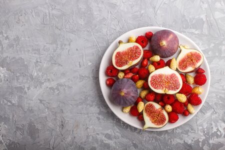 Fresh figs, strawberries and raspberries on white ceramic plate on gray concrete background. top view, flat lay, copy space.の写真素材