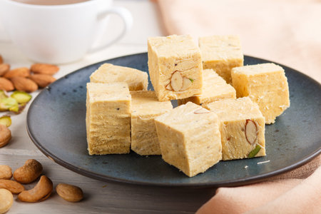 traditional indian candy soan papdi in a blue ceramic plate with almond, pistachio, cashew and a cup...
